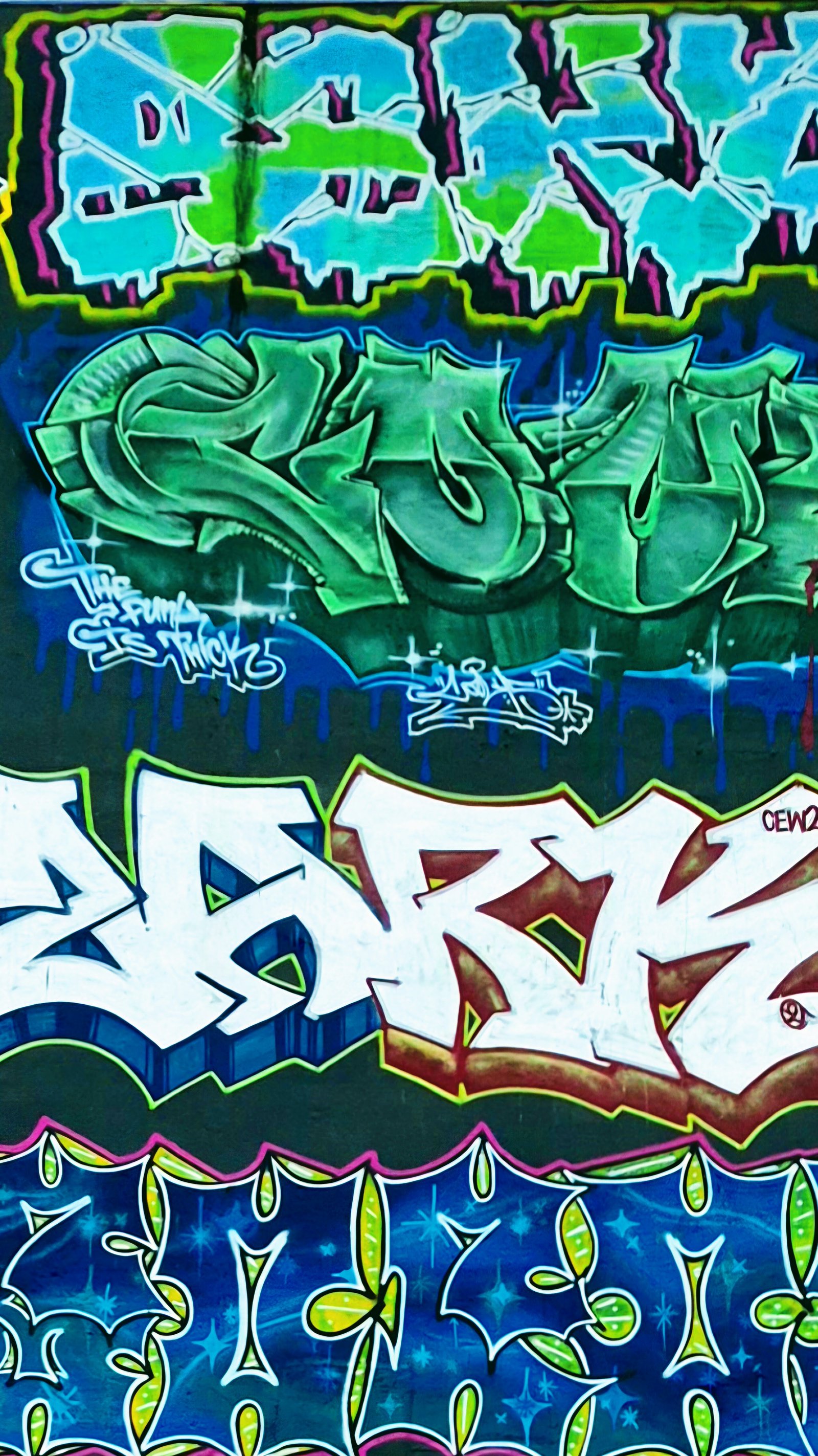 Green-toned graffiti pieces stacked on a dark wall